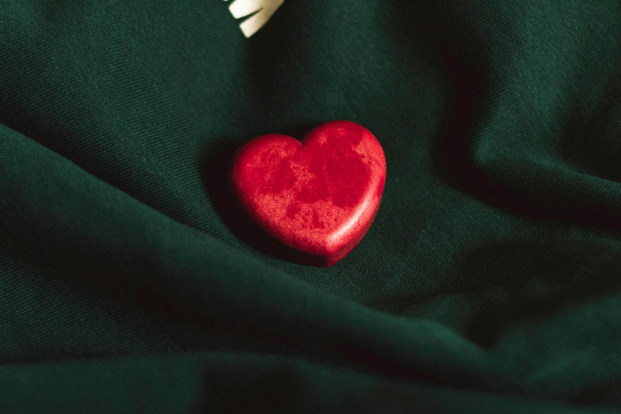 A vibrant red heart rests on a dark green fabric, symbolizing love.