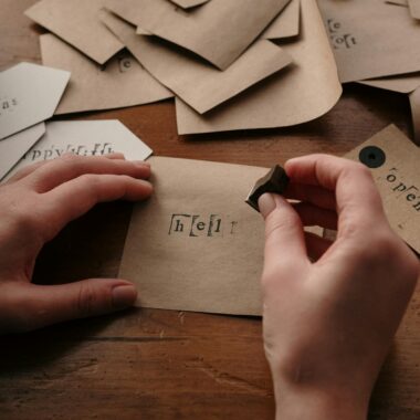 Hands stamping custom cards with love on a wooden desk.